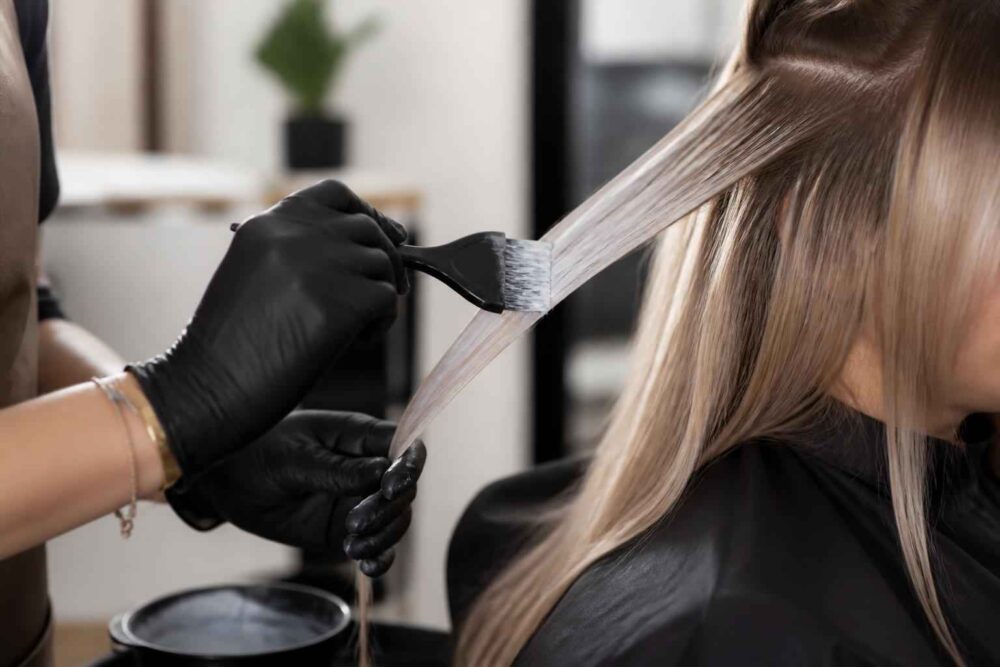 Rozjaśnianie pasma włosów w salonie Fryzjer nakłada rozjaśniacz pędzlem na wydzielone pasmo długich włosów klientki
